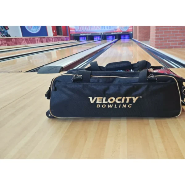 Velocity 3 Ball Triple Tote Black Gold bowling bag beside the lanes, gold trim and wheels visible
